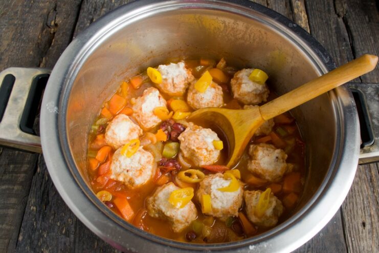 Cooking the Chicken Meatballs Directly in the Ragout Raw chicken meatballs being placed on top of the simmering vegetable ragout.
