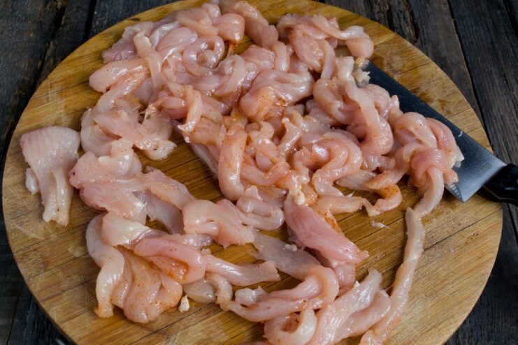 Thin strips of chicken fillet being fried in a hot pan.