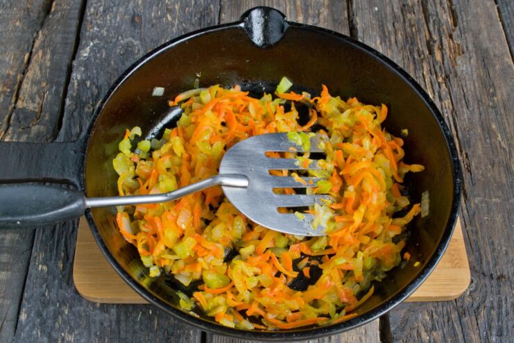 A mix of chopped onions, celery, and grated carrots being sautéed in a pan.