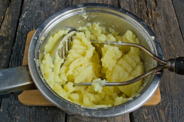 Freshly boiled potatoes being mashed in a pot to make a smooth puree.