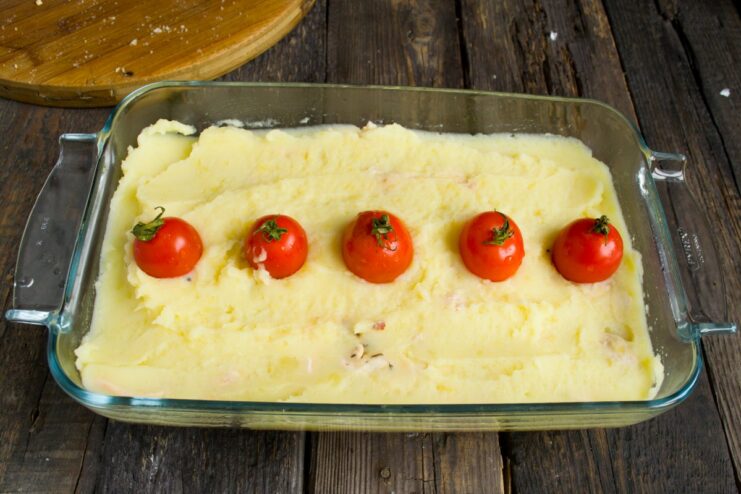 A row of cherry tomatoes being placed on top of the mashed potato layer.