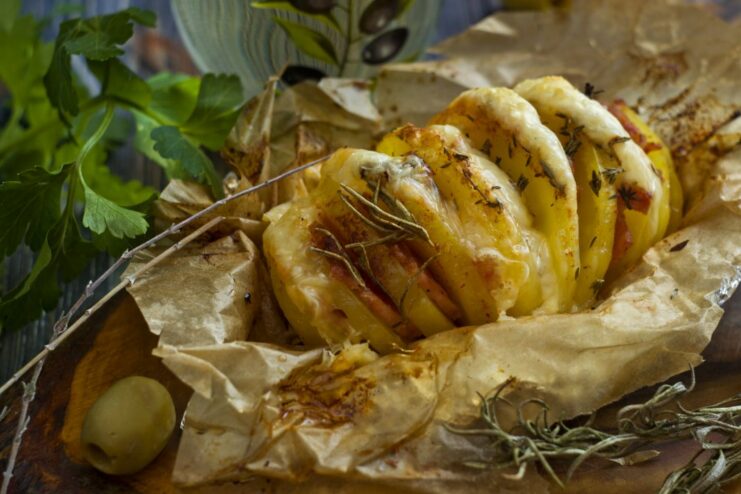 Delicious Baked Accordion Potato with Ham and Cheese A serving of baked accordion potato with ham and melted cheese, garnished with herbs.