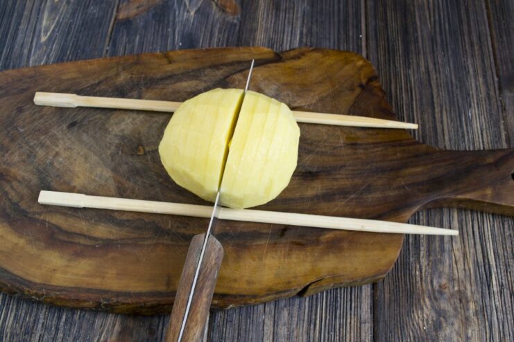How to Slice an Accordion Potato Without Cutting Through Slicing a potato placed between two wooden sticks to create an accordion effect.