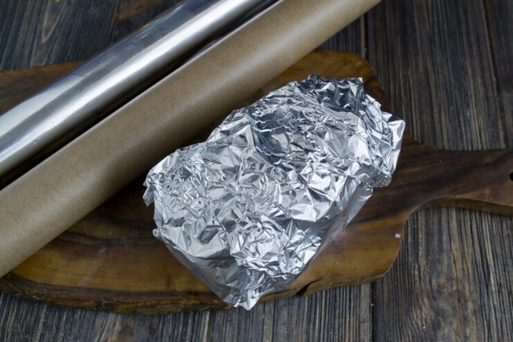 Step 7: Wrapping in Foil for Even Baking The parchment-wrapped potato being enclosed in a double layer of aluminum foil.