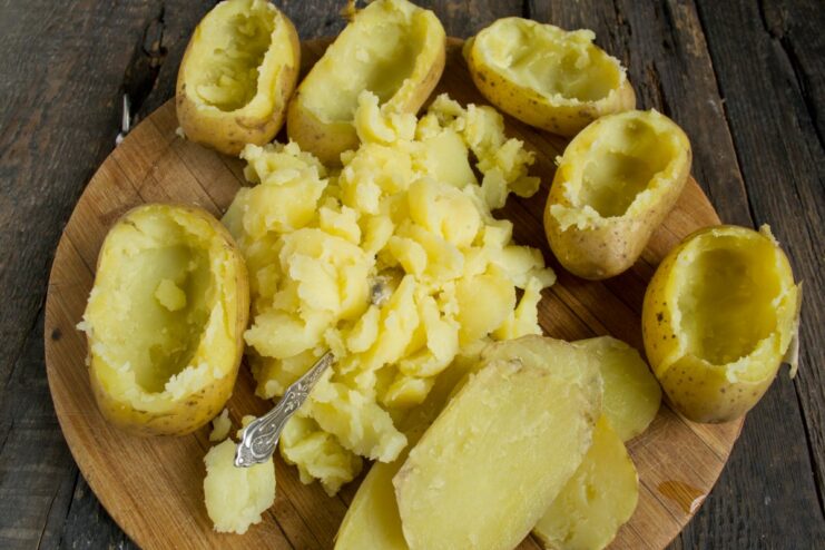 Step 2: Creating potato boats for stuffing A hand using a spoon to scoop out the flesh from a boiled potato half.