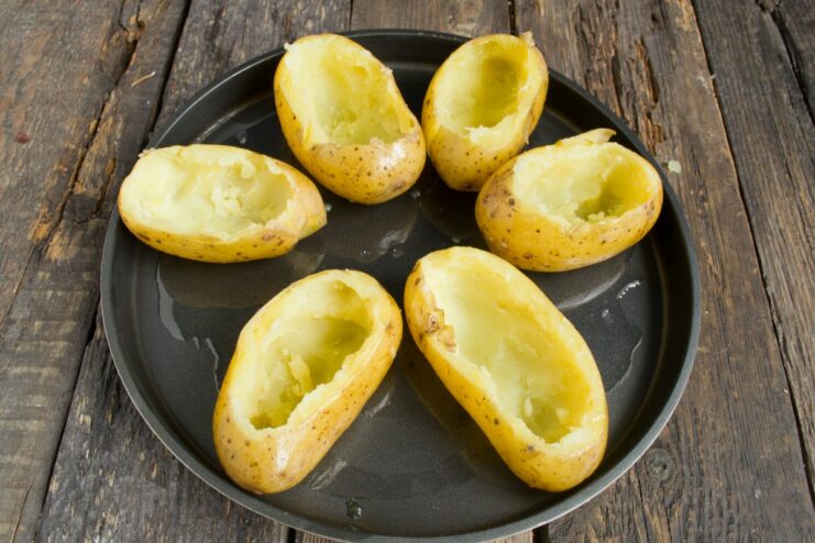 Step 6: Preparing potato skins for baking Hollowed-out potato skins being coated in oil on a baking sheet.