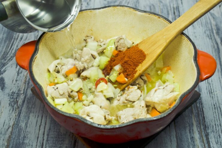 Adding Paprika and Water to Create a Savory Broth Stirring ground paprika into the chicken and vegetable mix before adding water.