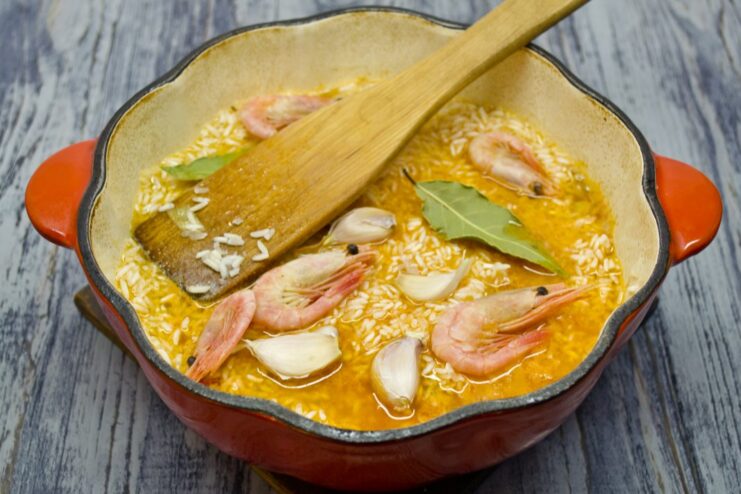 Layering the Final Ingredients Before Simmering Arranging frozen shrimp, whole garlic cloves, and bay leaves on top of the rice.