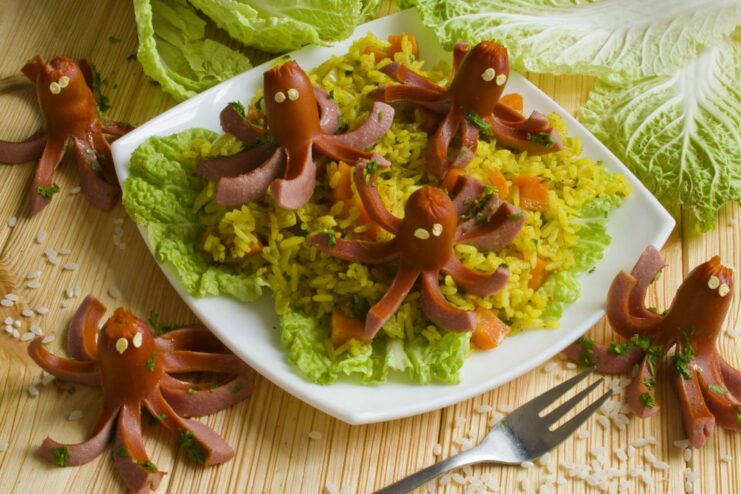 A bowl of freshly made plov with sausages cut to look like octopuses, garnished with cilantro.