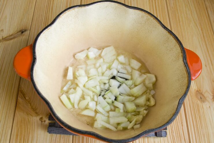 Step 1: Building the Flavor Base for Plov by Sautéing Onions Chopped onions being sautéed in a black braiser with hot oil.