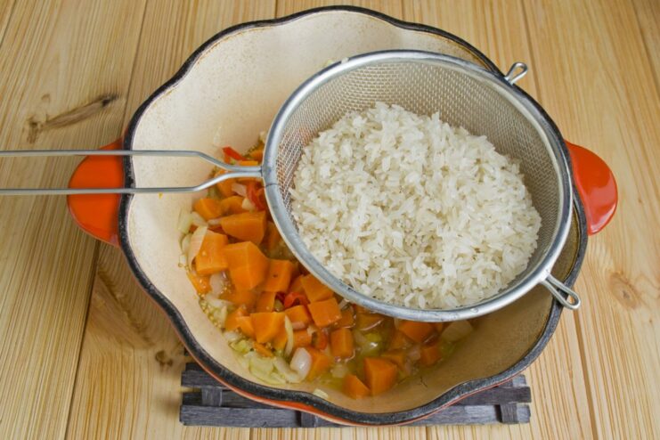 Toasting the Rice Grains to Enhance Nutty Flavor Rinsed long-grain white rice being toasted with sautéed vegetables in a braiser.