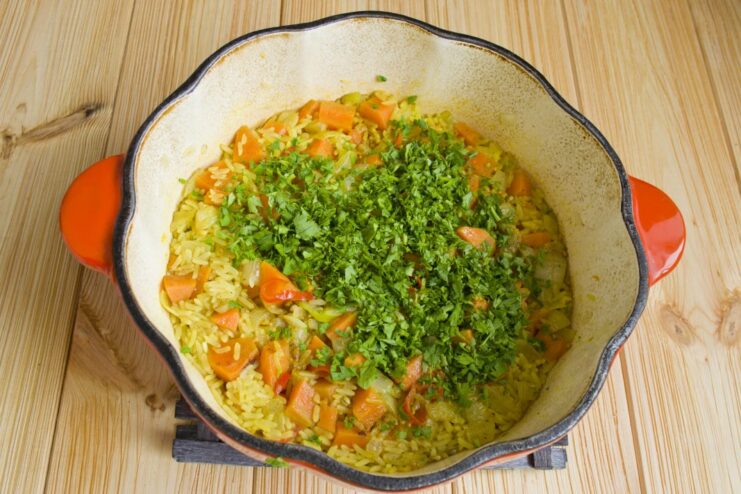 Finishing Touch: Adding Fresh Cilantro for Brightness Chopped fresh cilantro being added to the cooked rice in the braiser.