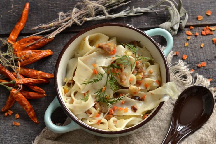 A white bowl filled with homemade noodles and mushroom sauce, garnished with fresh dill.