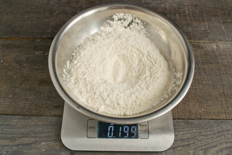 Step 1: Combining flour, water, and oil for the noodle dough A mound of flour in a bowl with a well in the center containing water and oil.