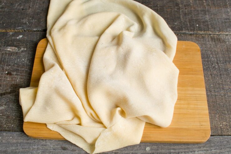 Step 3: How to roll out noodle dough very thinly A large, thin sheet of rolled-out noodle dough on a floured surface with a rolling pin.