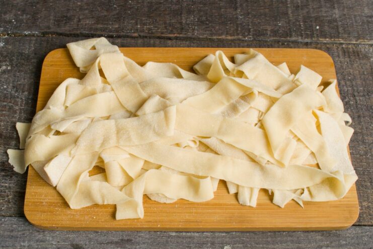 Step 4: Cutting the rolled dough into noodle strips A roll of dough being sliced into thin strips to create homemade noodles.
