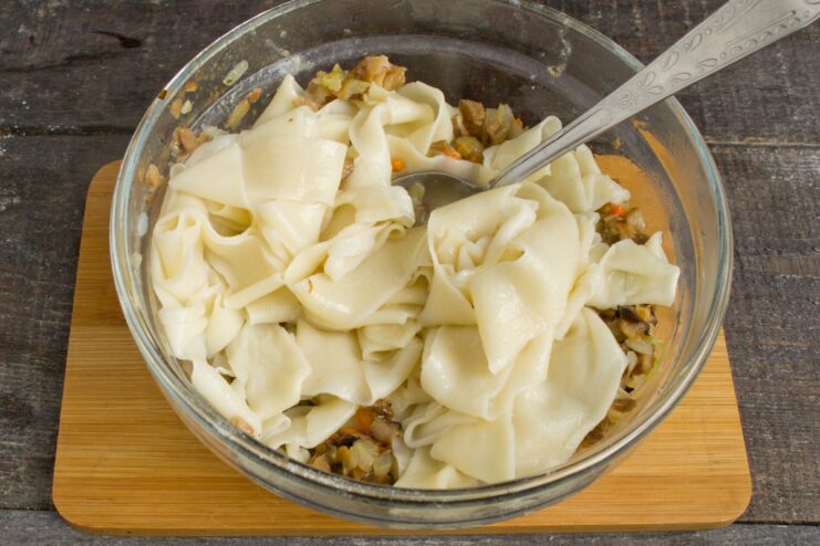Bringing it all together: Combining cooked noodles with the mushroom sauce Cooked homemade noodles being mixed with the savory mushroom sauce in a pan.