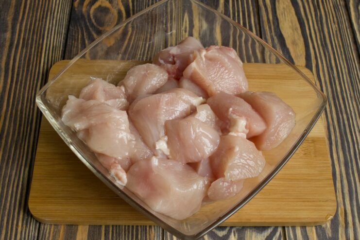 Cutting Chicken Breast into Cubes for Shashlik Raw chicken fillet being cut into large cubes on a cutting board.