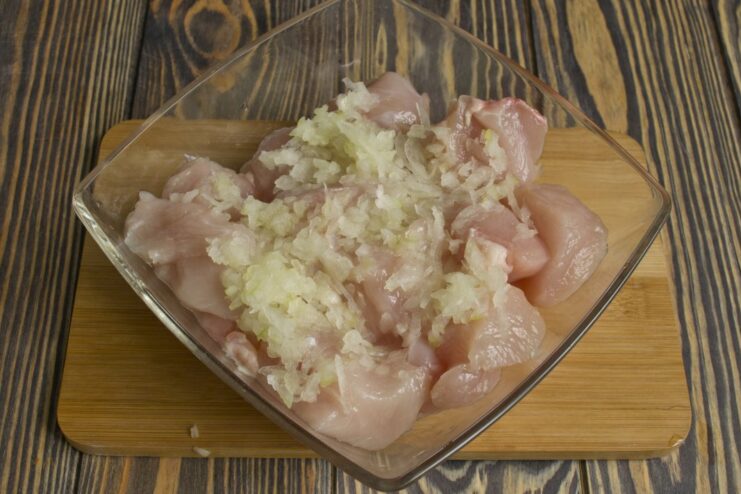 Marinating Chicken with Grated Onion Juice Grated onion being added to a bowl of cubed chicken for the marinade.