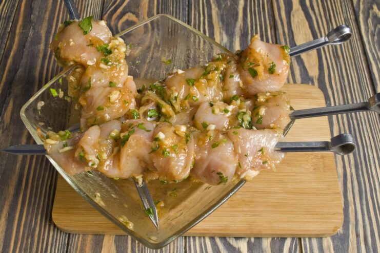 Preparing Chicken Skewers for the Oven Marinated chicken pieces being threaded onto metal skewers.