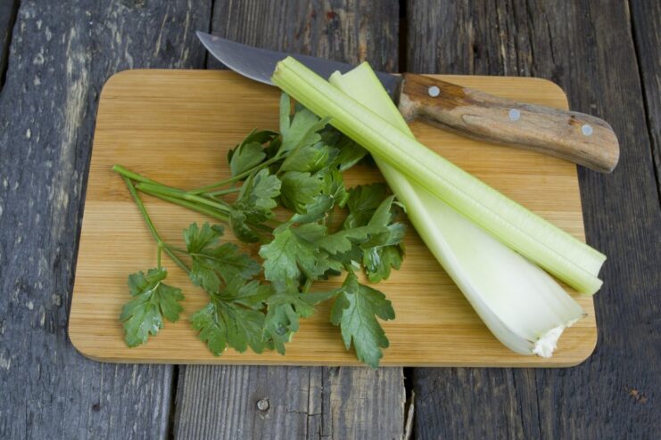 Adding Fresh Celery and Parsley to the Marinade Base Chopped celery stalks and fresh parsley being added to a blender.