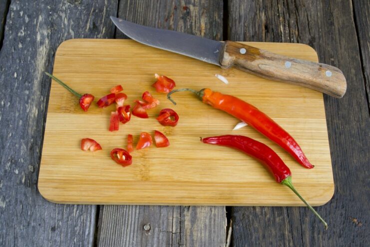 Adding a Kick: Slicing Chili for the Marinade A hand chopping a red hot chili pepper on a cutting board for the marinade.