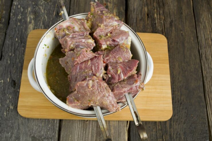Getting Ready to Grill: Skewering the Marinated Beef Marinated beef cubes being threaded onto long metal skewers.