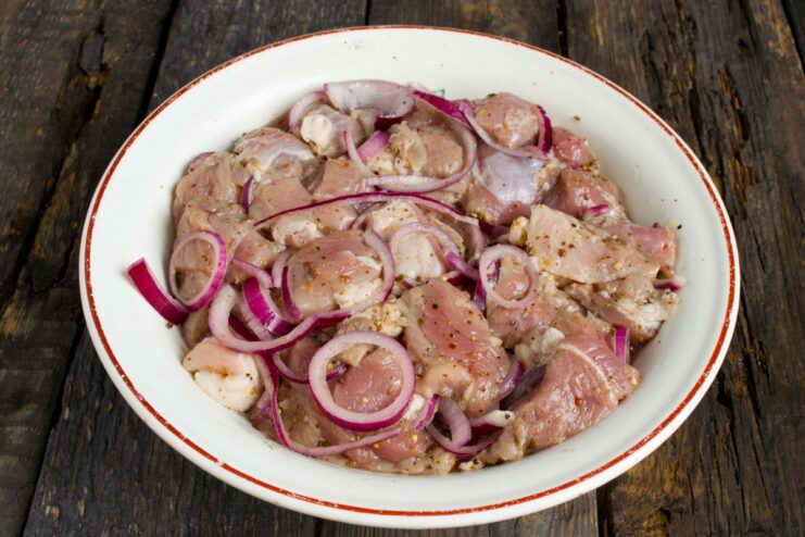 Marinating the Pork for Maximum Flavor A bowl of cubed pork mixed with sliced red onions and marinade.