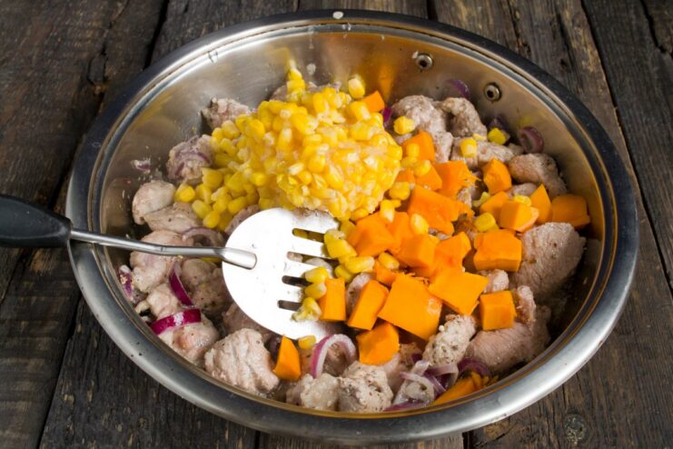 Adding Vegetables to the Pork Filling Canned corn and diced pumpkin pulp being added to the frying pork in a pan.