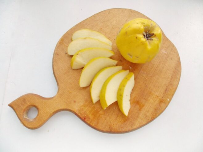 How to Prepare Quince for Roasting A hand slicing a cored quince into wedges on a cutting board.