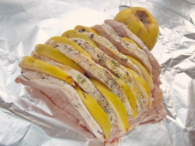 Stuffing the Pork with Aromatic Quince Quince slices being inserted into the scores of a seasoned piece of pork.
