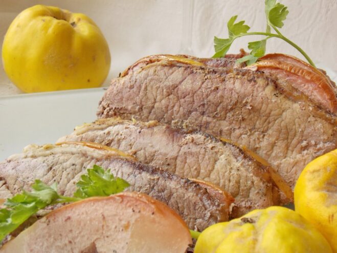 A plate of sliced pork baked with quince, garnished with fresh herbs.