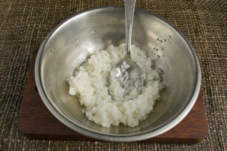Seasoning Cooled Sushi Rice with Vinegar Mixture A bowl of cooked rice being mixed with a liquid marinade.