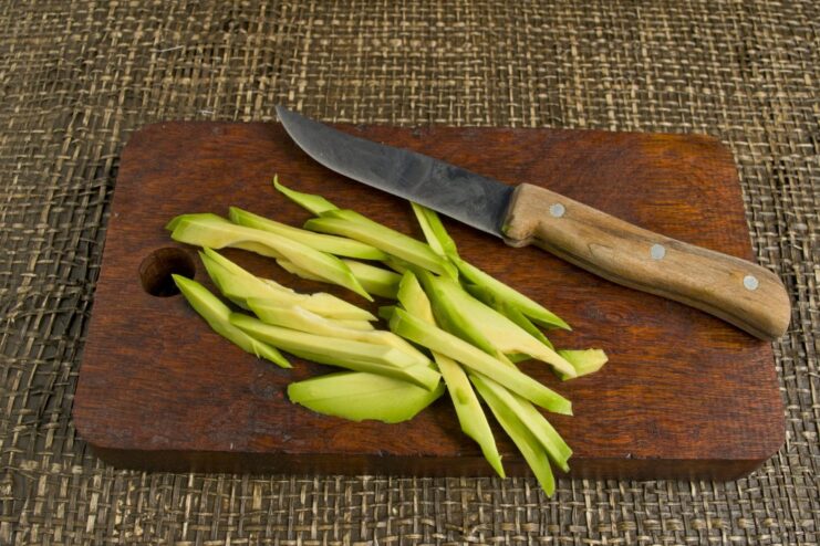 Slicing Avocado into Perfect Strips for Temaki Filling A peeled avocado being sliced into thin strips on a cutting board.
