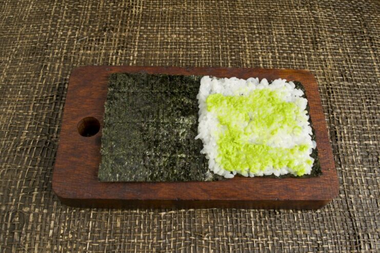 Adding a Touch of Spicy Wasabi to the Sushi Rice A finger spreading a thin layer of green wasabi paste on the sushi rice.