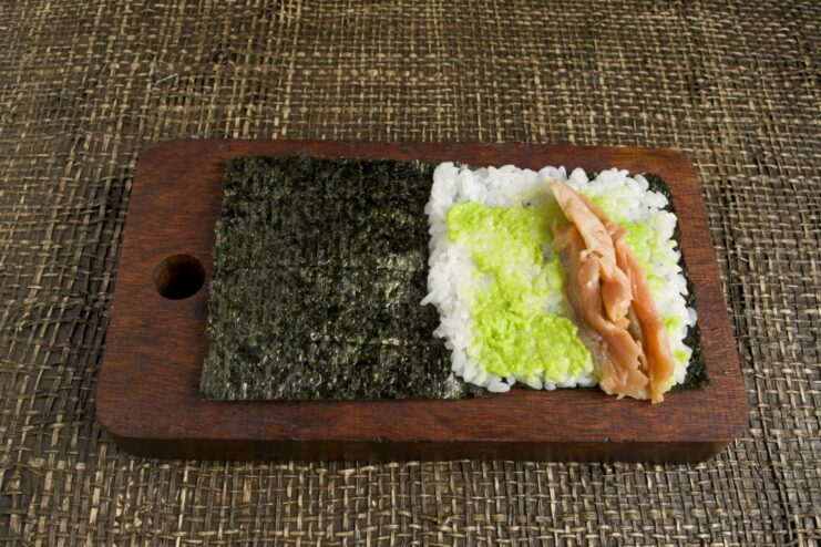 Layering Sliced Trout for the Temaki Sushi Filling Strips of salted trout being placed on top of the rice on a nori sheet.