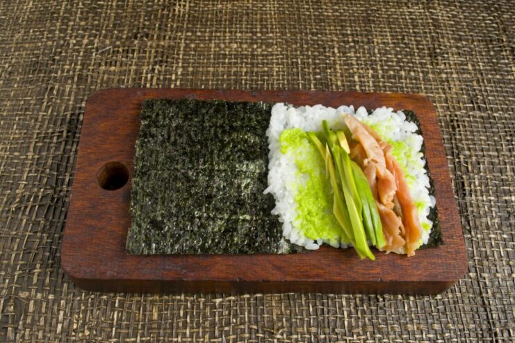 Adding Creamy Avocado Slices to the Temaki Filling Sliced avocado being placed next to the trout on the sushi rice.