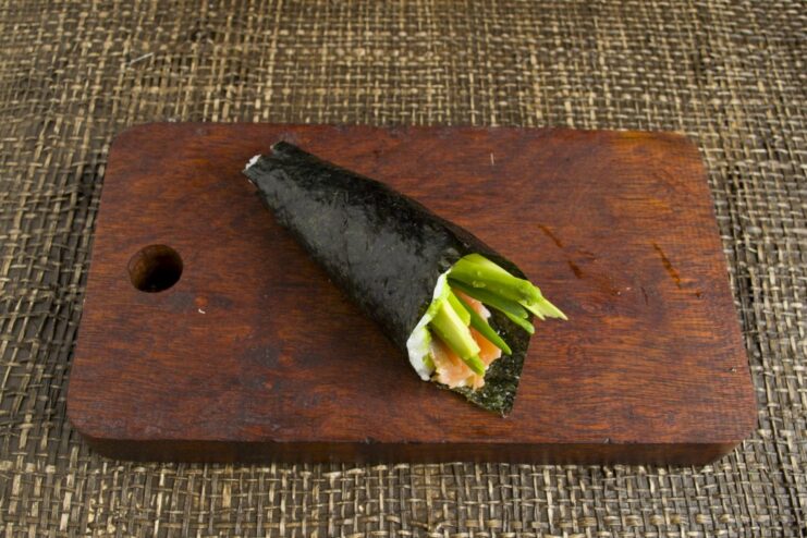 How to Roll Nori into the Perfect Temaki Cone Shape A nori sheet with fillings being rolled by hand into a cone shape.