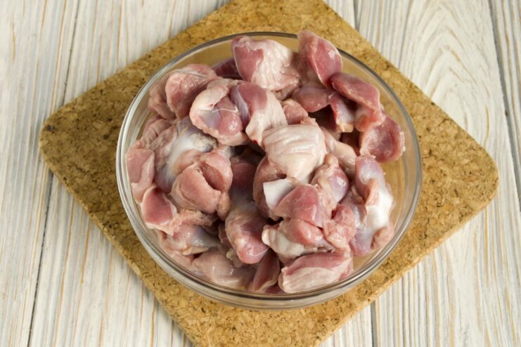 Step 1: Preparing the chicken gizzards by cleaning, rinsing, and patting them dry. Raw, cleaned chicken gizzards on a cutting board, ready for cooking.