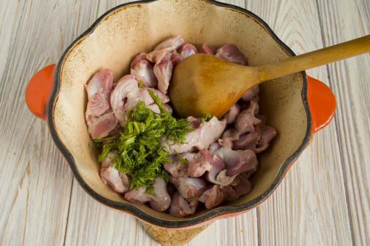 Searing the gizzards with garlic and herbs to build a flavorful base. Chicken gizzards, garlic, and dill being sautéed in a Dutch oven.