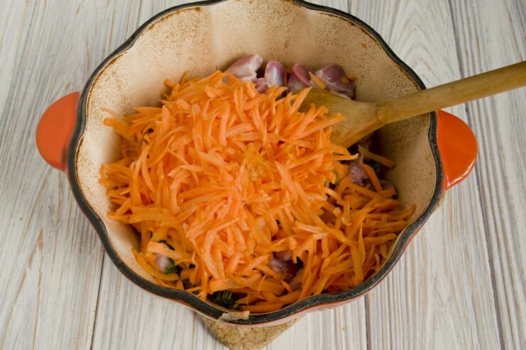 Adding aromatics like onion, carrot, and spices to the pot. Sliced onions, grated carrots, and bay leaves added to the gizzards in the pot.