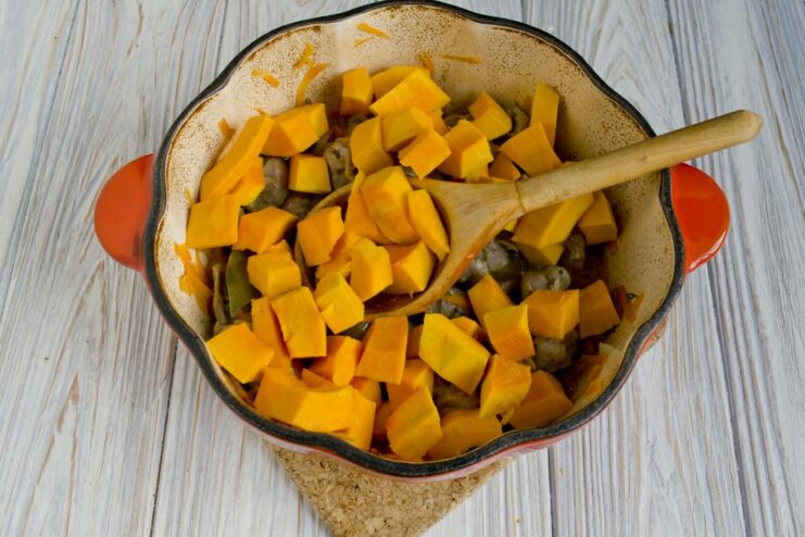 Adding cubed pumpkin to the stew for the final stage of cooking. Cubed pumpkin being added to the stewed chicken gizzards in the pot.