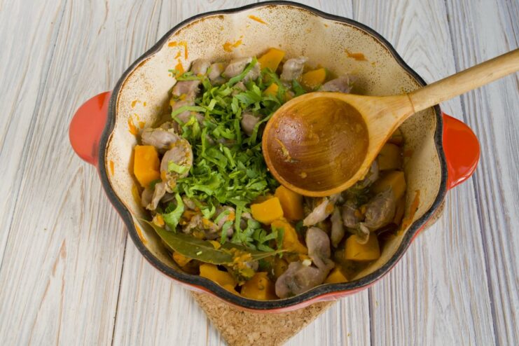 Finishing the dish with a sprinkle of fresh herbs for a burst of freshness. Freshly chopped parsley being added to the finished stew in the pot.