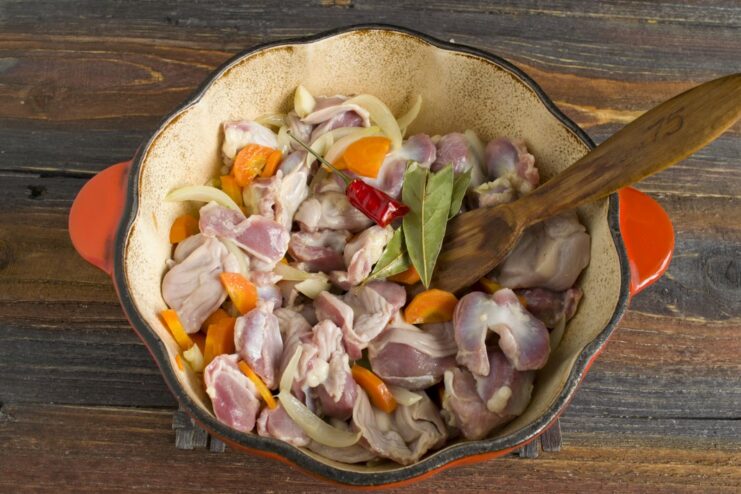 Layering Aromatics: Gizzards, Chili, and Bay Leaf Chicken gizzards, a red chili pepper, and bay leaves added to the sautéed vegetables in a pot.