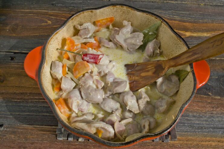 Creating the Creamy Sauce for the Stewed Gizzards A creamy sour cream and flour mixture being poured over chicken gizzards and vegetables in a pan.