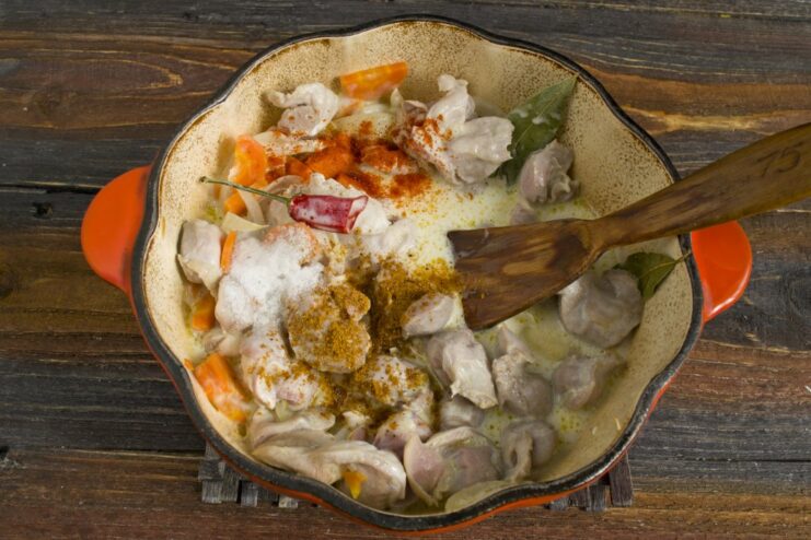 Seasoning the Dish with Paprika, Curry, and Salt Spices like paprika and curry powder being added to the chicken gizzard stew to enhance the flavor.