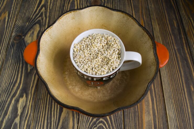 Measuring Pearl Barley for the Recipe A white mug filled with dry pearl barley grains.