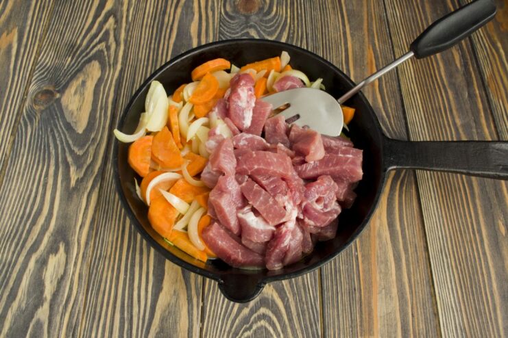 Browning Pork with Onions and Carrots Pieces of pork being browned in a pan with onions and carrots.