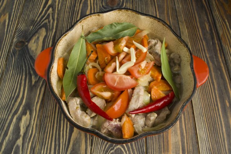 Adding Aromatics and Tomatoes to the Dish Chili peppers, tomatoes, and bay leaves being added to the pearl barley with meat.