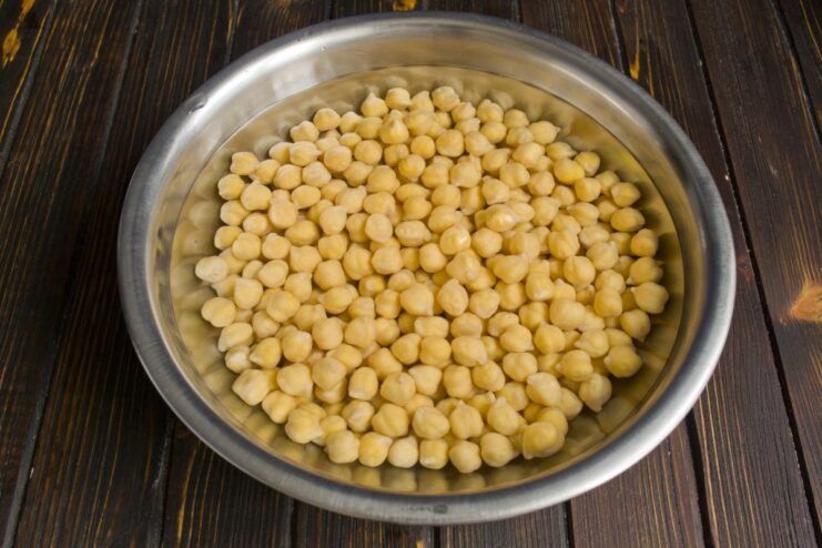 Soak chickpeas overnight to ensure they cook evenly and are easy to digest A bowl of dry chickpeas being soaked in clear water.